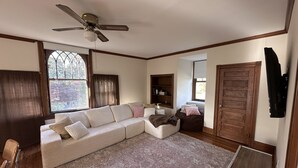 A living room with a sectional sofa, a ceiling fan, a wooden door, and a window with curtains. - Sun Filled 2-bedroom in Victorian Home; pleasant Wyndmoor / Chestnut Hill Area (Wyndmoor)