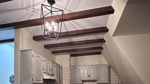 Una cocina con vigas de madera, armarios blancos, estufa y cafetera.