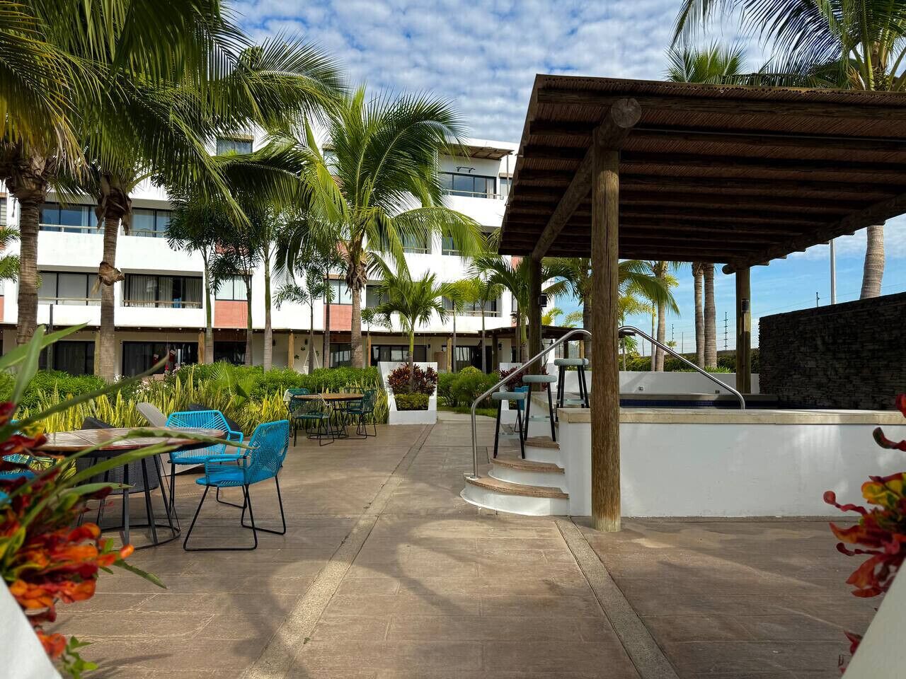Une cour d’hôtel avec des espaces de détente en plein air, des palmiers et un escalier menant à un espace piscine.