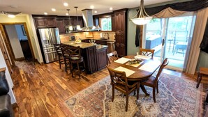 A spacious kitchen with a central island, dark wooden cabinets, stainless steel appliances, and a dining area with a large rug and chairs. - Luxurious Littleton Living with Gourmet Kitchen, Huge Deck and Shared Backyard (Littleton)