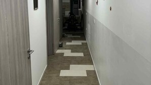 A hallway with a wooden floor and white walls, leading to a room with a bed and a chair. - Comfort Apartment Luna (Varazdin)