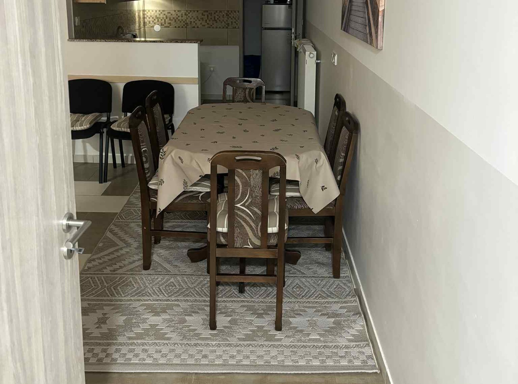 A dining area with a table, chairs, and a kitchen in the background.