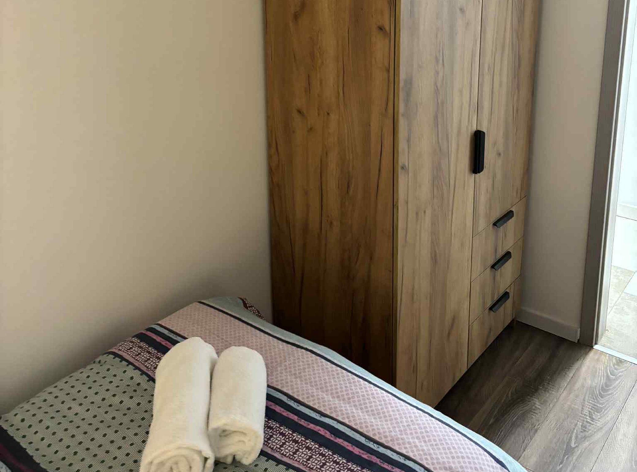 A bedroom with a bed, a wooden wardrobe, and a window.