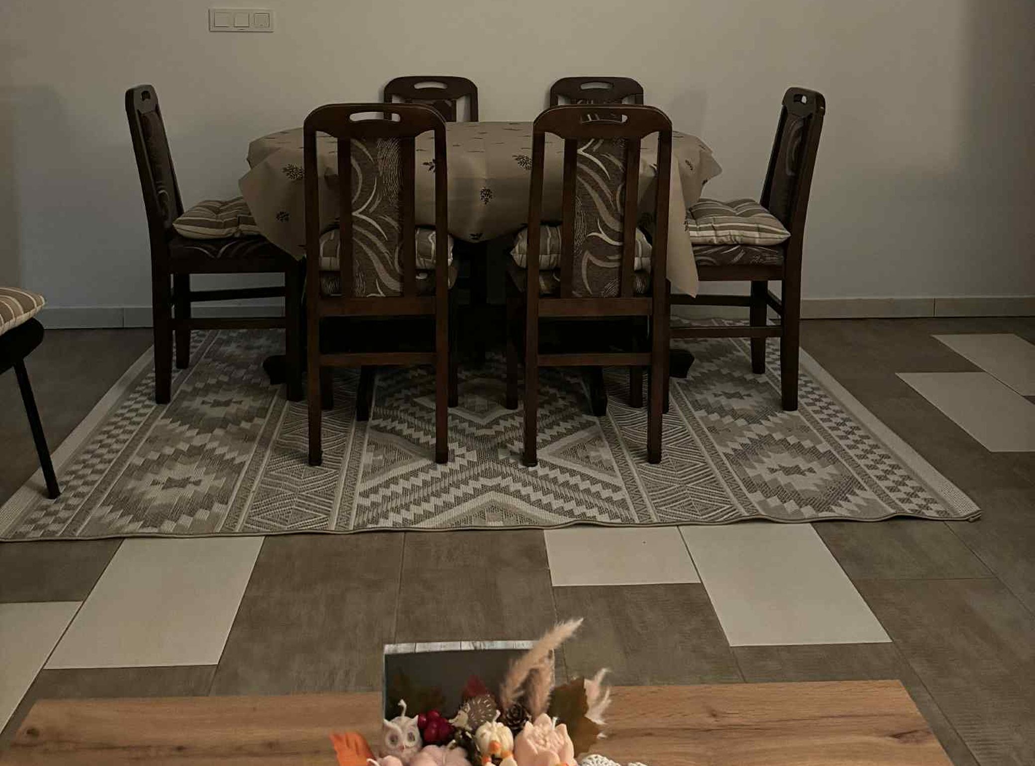 Un comedor con una mesa y cuatro sillas, un tapete estampado y una mesa de centro de madera con objetos decorativos.