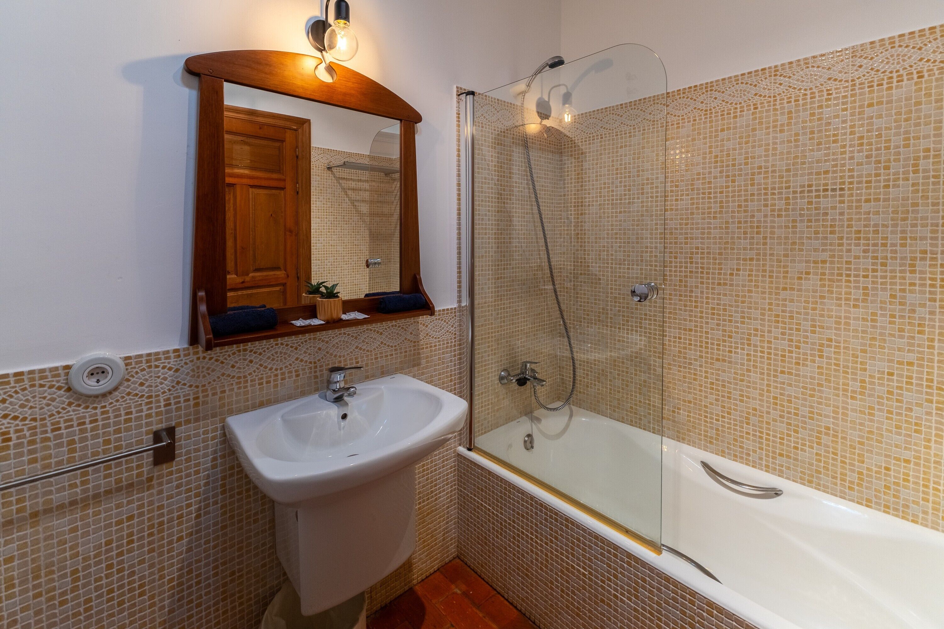 A bathroom with a sink, mirror, shower, and tiled walls.