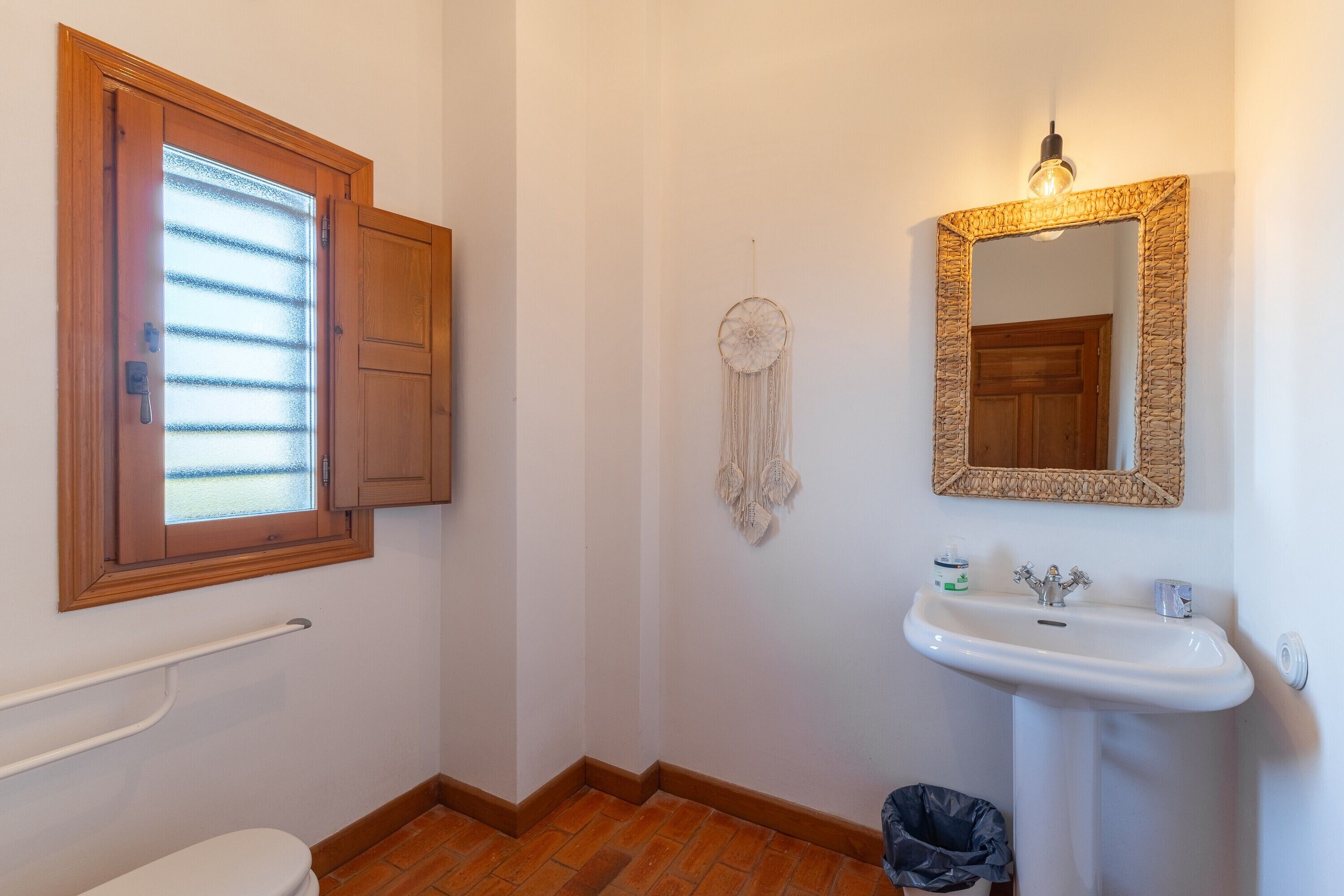 A bathroom with a wooden door, a window, a white sink, a mirror, and a towel rack.