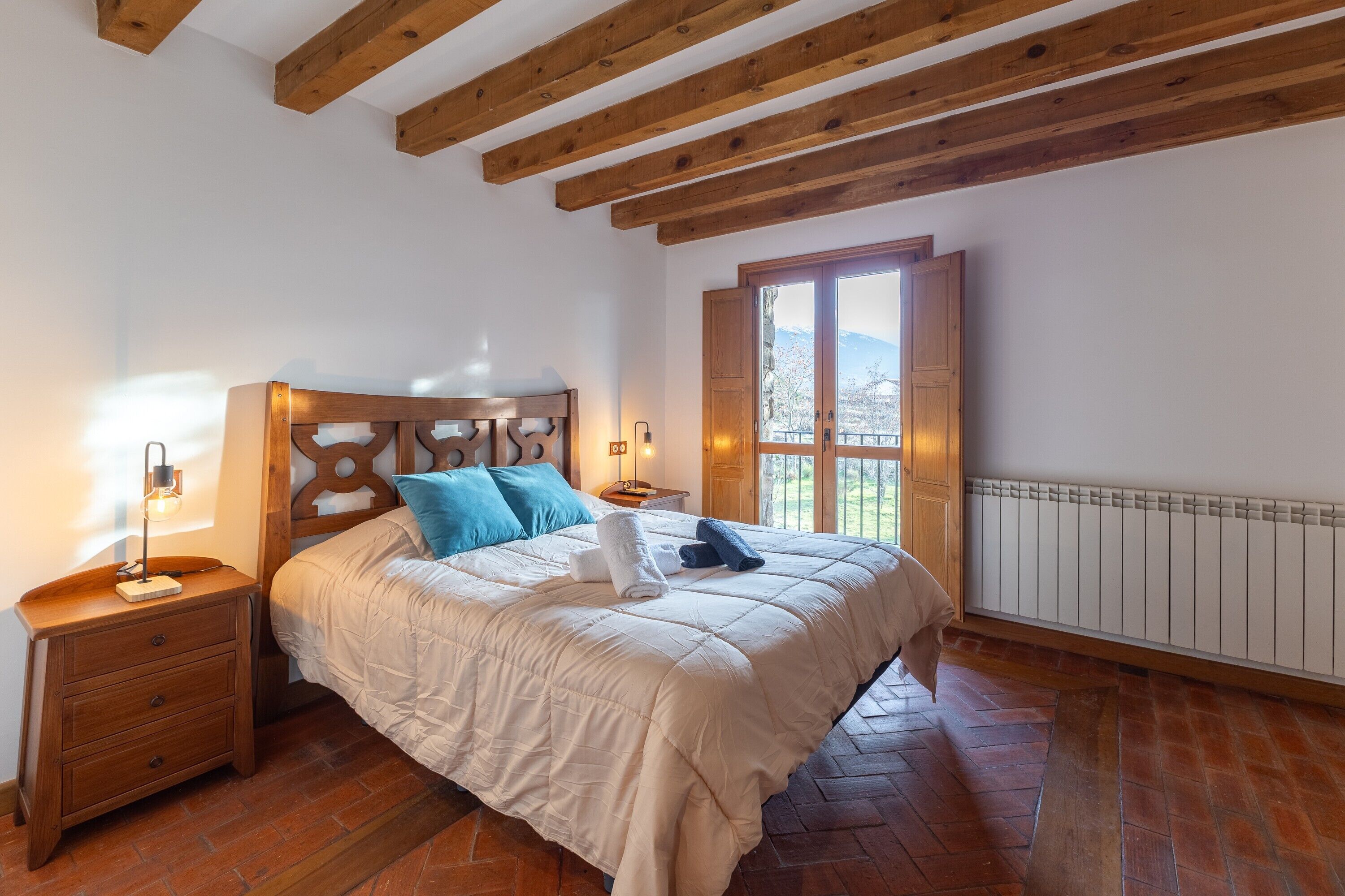 Un dormitorio con techo de madera, una cama con edredón blanco, una mesita de noche con lámpara y una ventana con vistas.