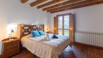Un dormitorio con techo de madera, una cama con edredón blanco, una mesita de noche con lámpara y una ventana con vistas.