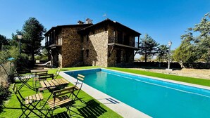 Una casa de piedra con piscina, mobiliario de exterior y cielo despejado.