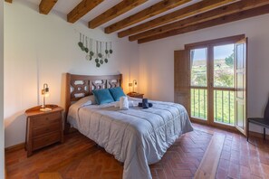 Una camera da letto con testiera in legno, un letto con biancheria da letto bianca, un comodino con una lampada e una finestra vista verde.