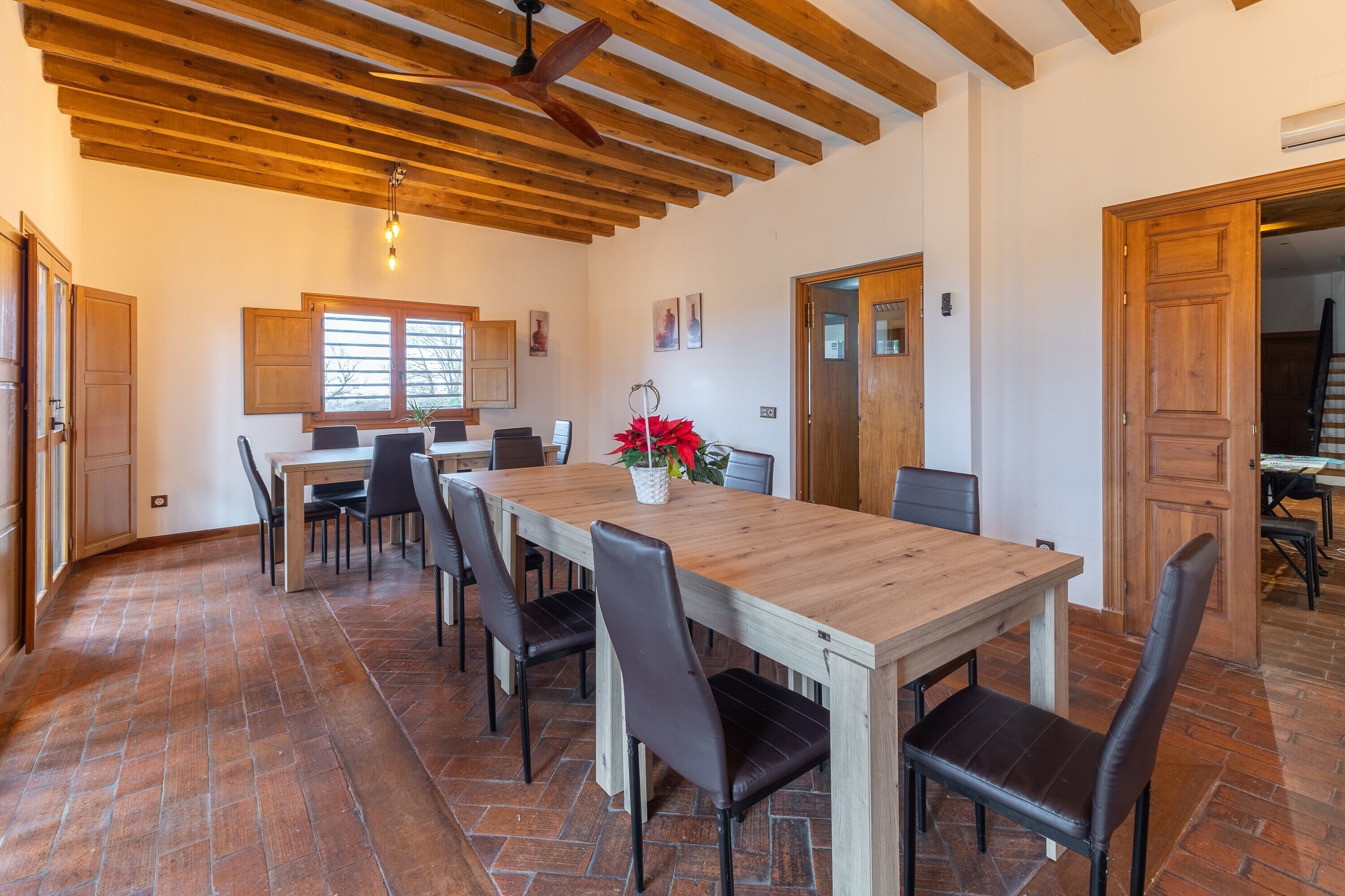 Zona pranzo con tavolo e sedie in legno, ventilatore a soffitto e pavimento piastrellato.