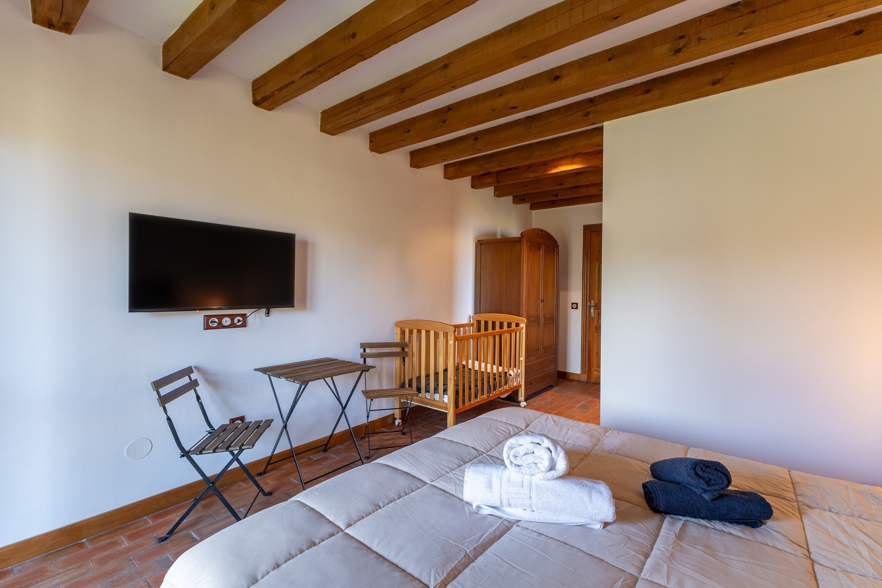 Une pièce comprenant un lit, un berceau, une télévision, une table et une chaise.
