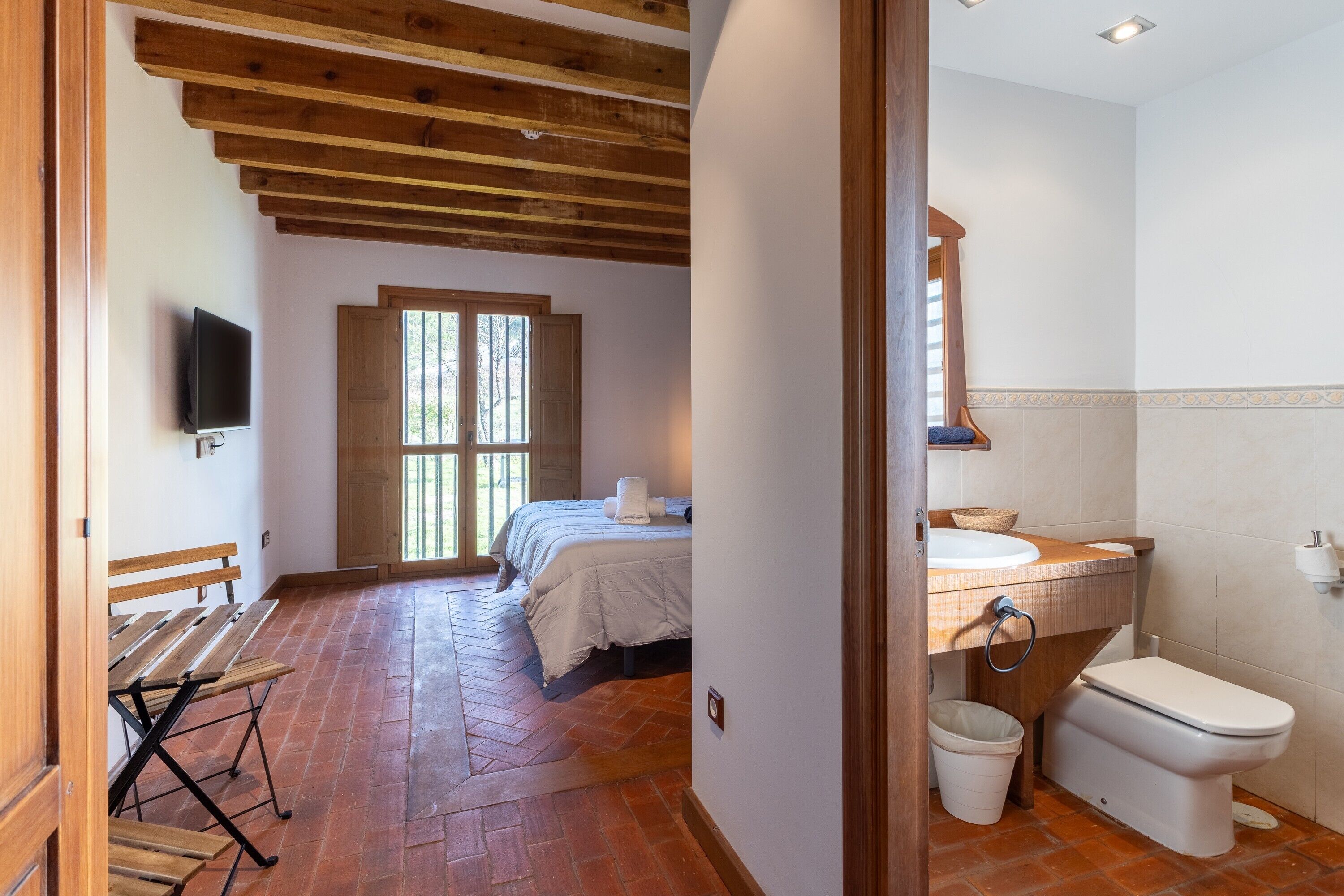Un dormitorio con una cama, un banco de madera, un televisor y una ventana.
