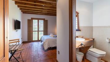 Un dormitorio con una cama, un banco de madera, un televisor y una ventana.