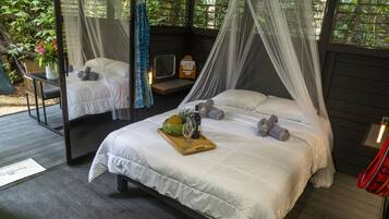 Un dormitorio con cama de dosel, una mesita con fruteros y una botella, y una silla.