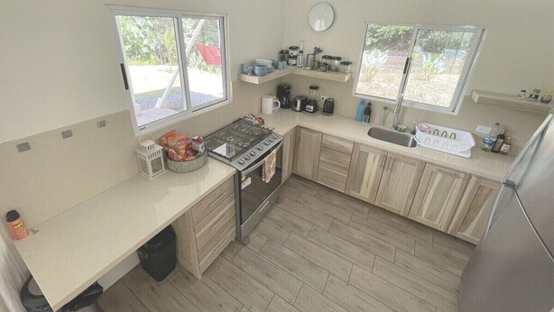 Cocina compacta con estufa, lavamanos y dos ventanas.