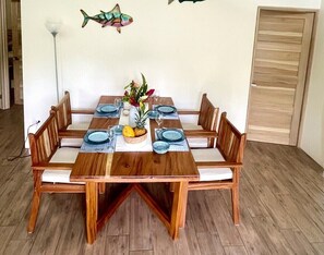A dining table with six chairs, a fruit bowl, and a vase with flowers.