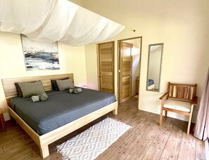 A bedroom with a bed, a wooden chair, a mirror, and a door.