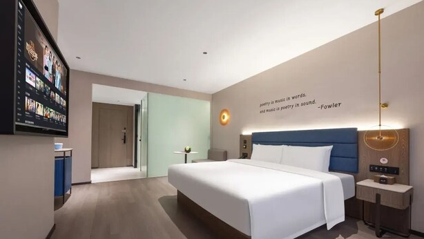 A modern hotel room with a large bed, a flat-screen TV mounted on the wall, a bedside table with a lamp, and a quote on the wall. - MANNSIC Hotel- Shenzhen Haishang Shijie (Shenzhen)