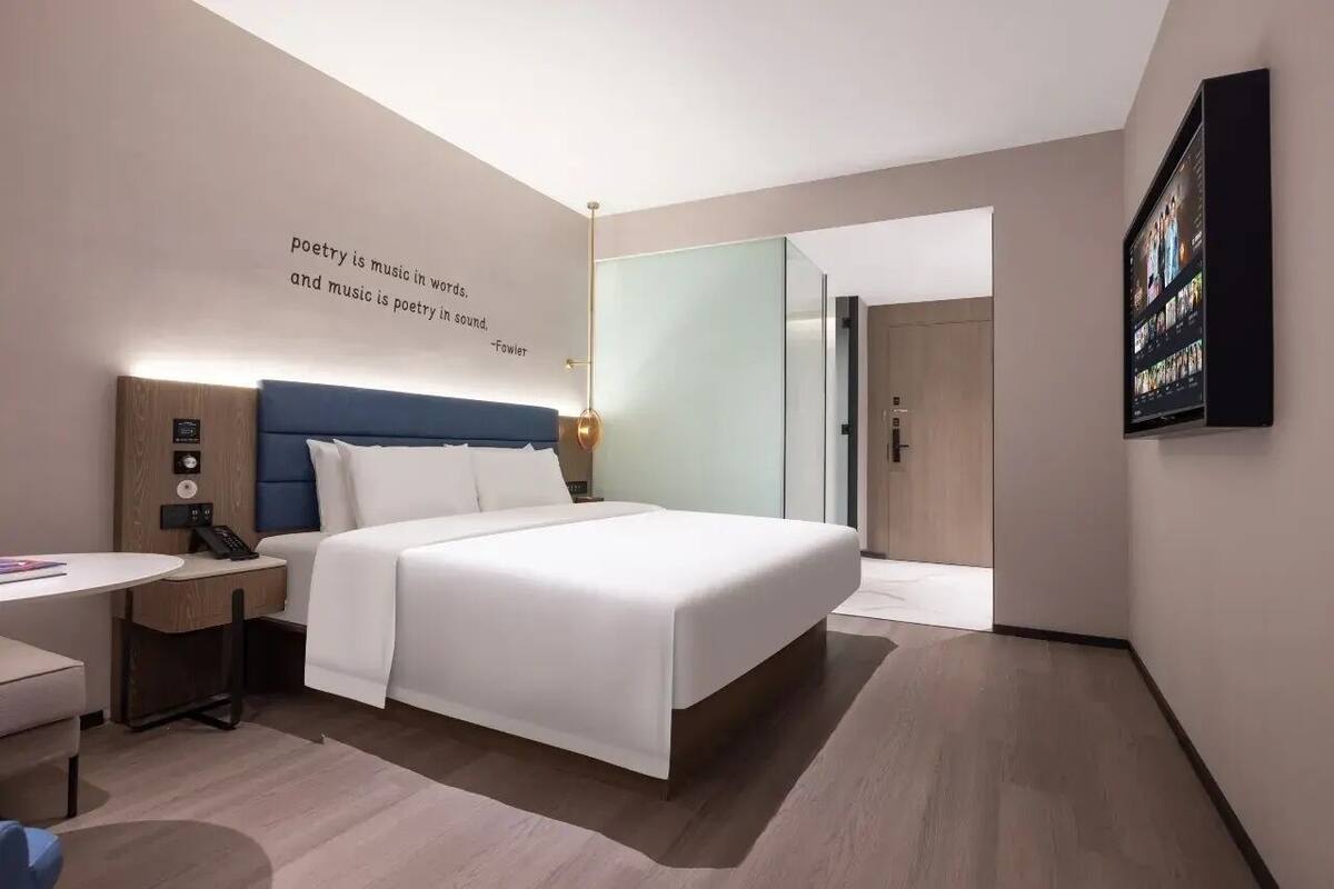 Une chambre d’hôtel moderne avec un grand lit, des tables de chevet, un bureau et un téléviseur fixé au mur.