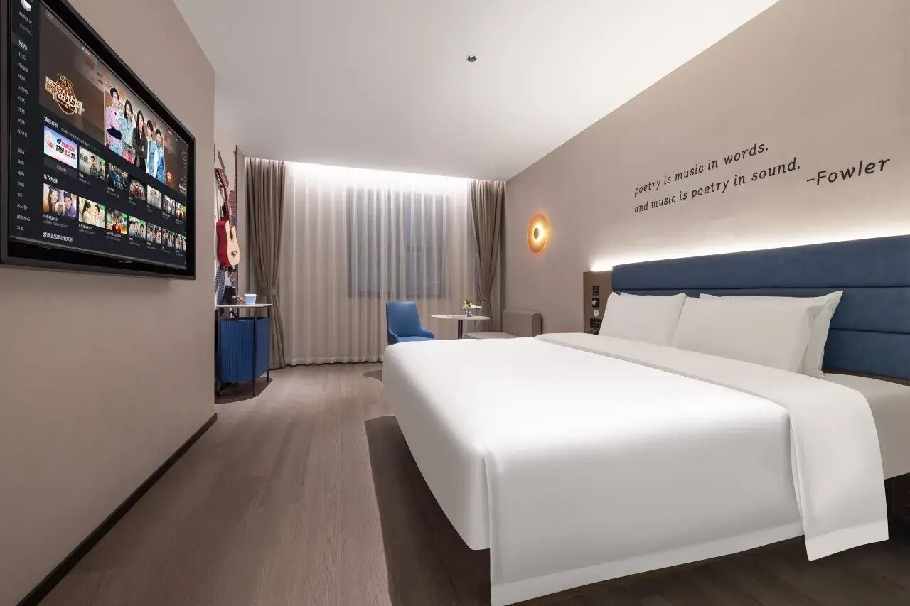 Habitación de hotel con una cama grande, un televisor en la pared, una mesita pequeña y una silla.