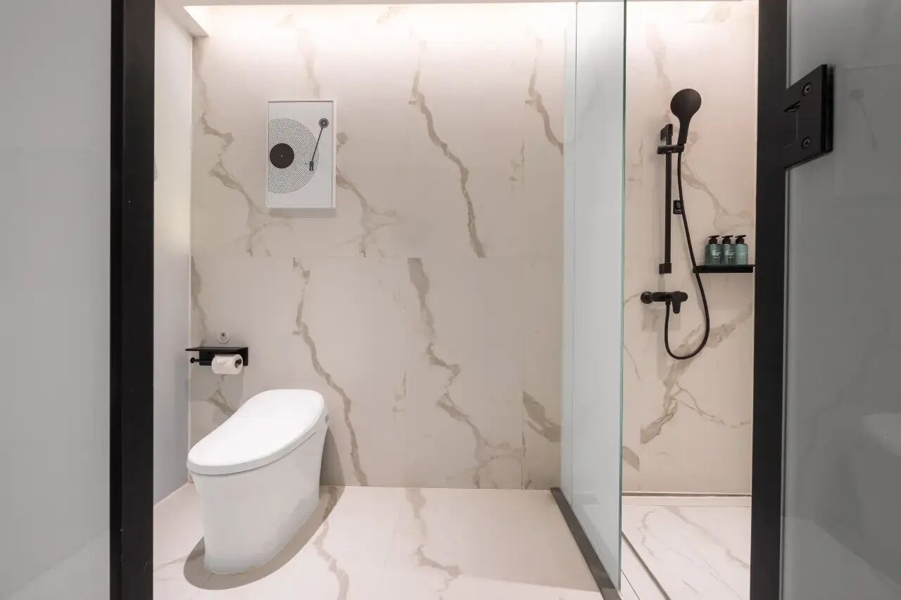 A modern bathroom with a toilet, a shower with a handheld showerhead, and a marble-patterned wall.