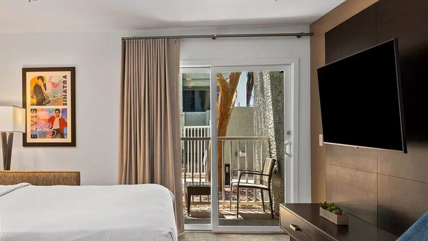 A hotel room with a bed, a TV, a painting, and a sliding glass door to an outdoor area. - Worldmark Tropicana for NFR Rodeo & WSTR (Las Vegas)