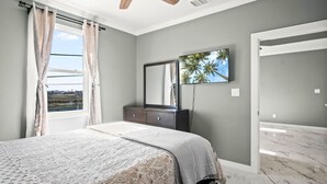 Quarto com cama, cômoda, televisão e vista para palmeiras.
