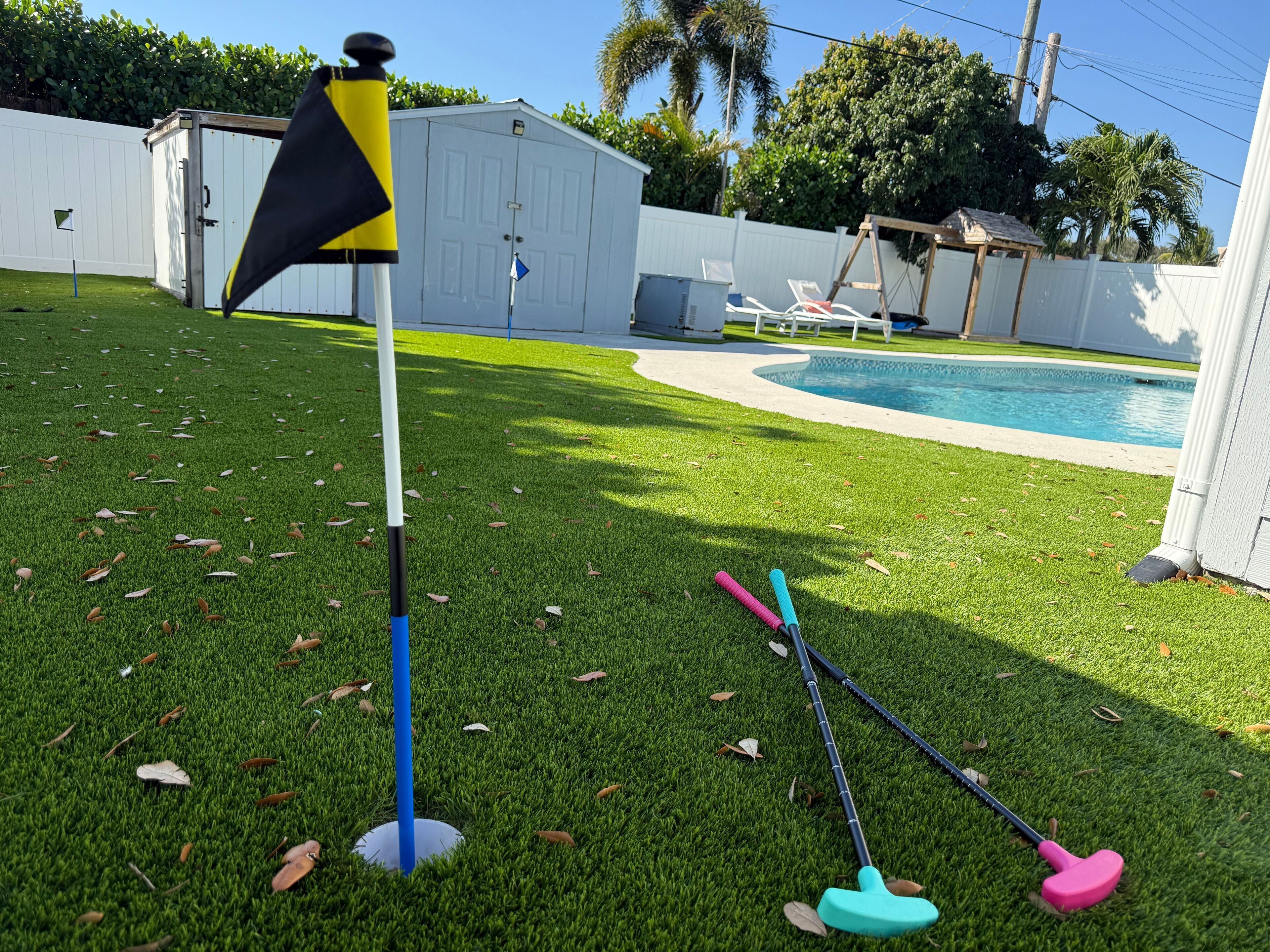 Ein Garten mit Pool, einer Flagge und zwei Golfschlägern auf dem Rasen.