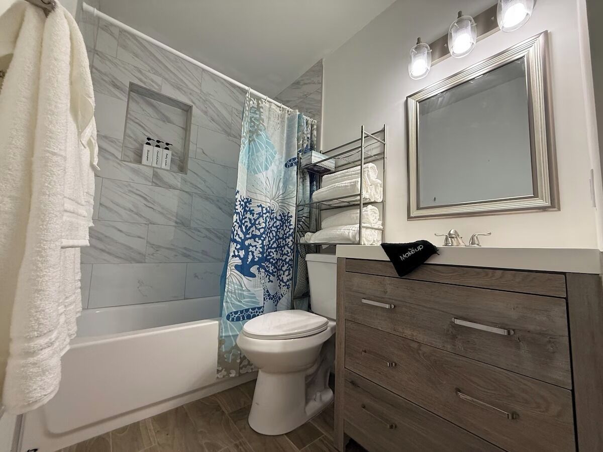 A bathroom with a bathtub, toilet, vanity with drawers, a mirror, and a shower curtain.