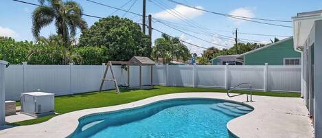 A swimming pool with a white fence, a ladder, and a small shed in a backyard.