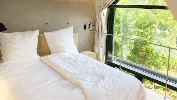 A bedroom with a large bed, a concrete headboard, and a view of greenery through a window. - Burgstrasse Apartment West with garden and sauna (Altleiningen)