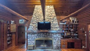 A log cabin interior with a stone fireplace, wooden ceiling beams, and a television mounted above it. - Secluded 8 acre lakefront resort on Grand Portage Lake. (Mercer)