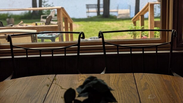 A wooden table with a potted plant, a window with a view of a lake and outdoor seating area. - Secluded 8 acre lakefront resort on Grand Portage Lake. (Mercer)