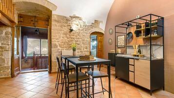 Una cocina con paredes de piedra, una mesa de madera y sillas, una encimera negra y una lámpara colgante.