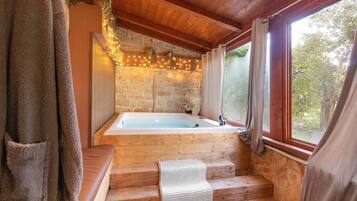 Una cabaña de madera con pared de piedra, un banco de madera, un tapete blanco tejido y una ventana con cortinas.