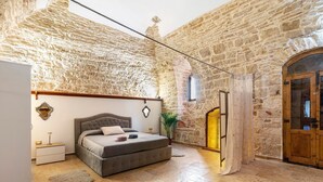 A bedroom with a stone wall, a bed, a nightstand, a plant, and a wooden door. - Luxury House 'Apulia' with Wi-Fi (Toritto)