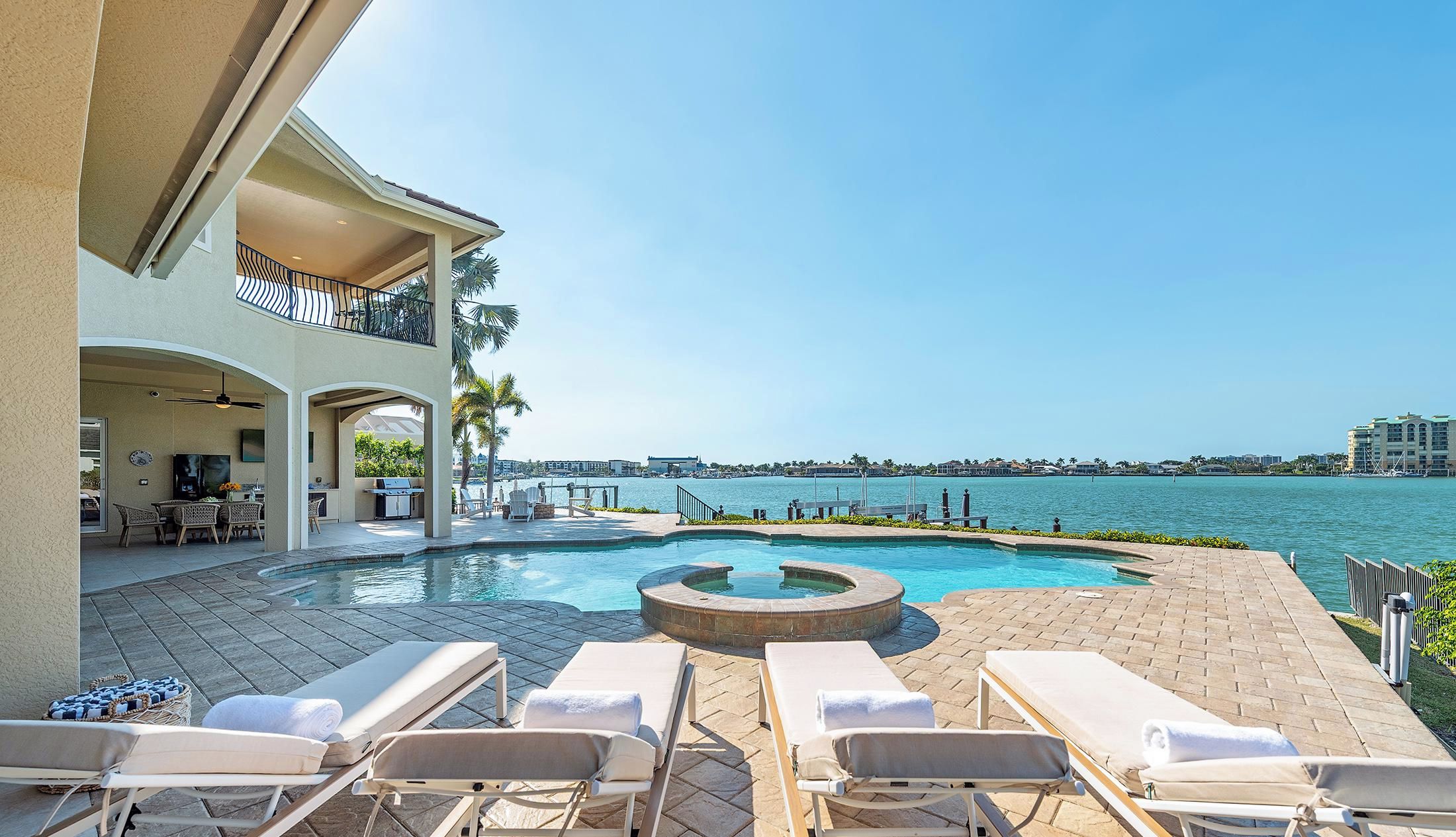A pool area with lounge chairs, a hot tub, and a view of the water.