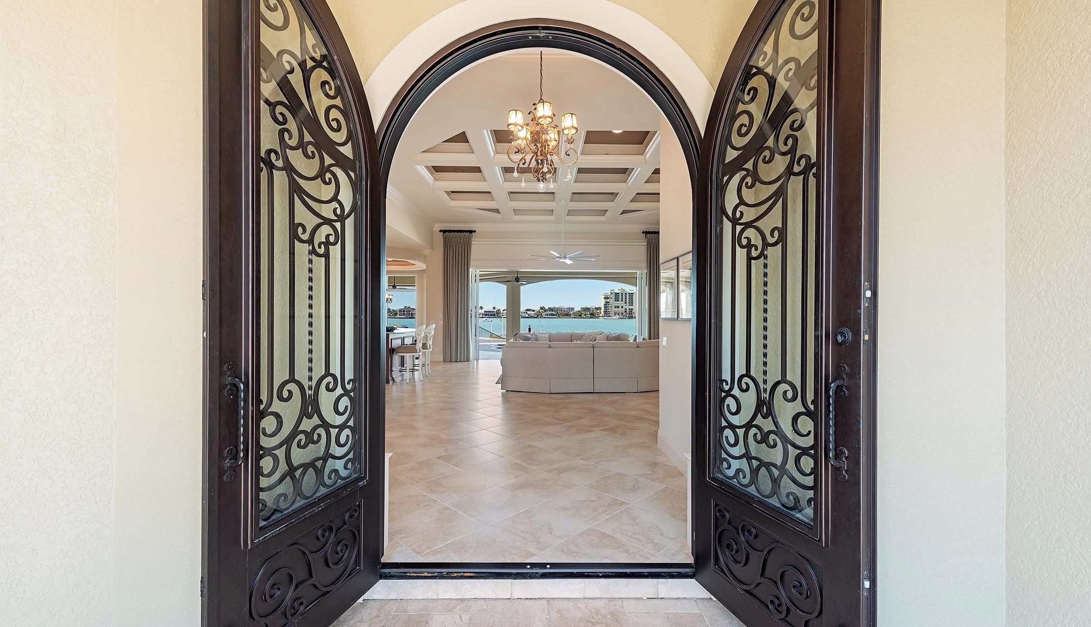 A grand entrance with a chandelier, a view of a living area with a sofa, and a dining area with chairs.