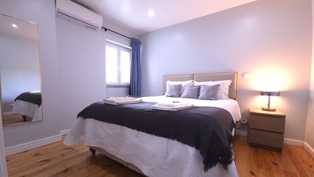 Un dormitorio con cama, mesita de noche, lámpara y ventana con cortinas.