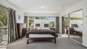 A bedroom with a large bed, a dresser, and a window with curtains. - Harbour Crest Retreat - Lyttelton Holiday Home (Lyttelton)