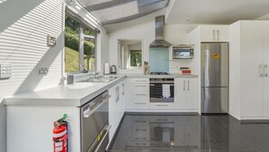 A modern kitchen with a central island, stainless steel appliances, and a view of greenery outside. - Harbour Crest Retreat - Lyttelton Holiday Home (Lyttelton)