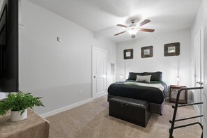 Et soveværelse med seng, ventilator, kommode, en plante og en stige.