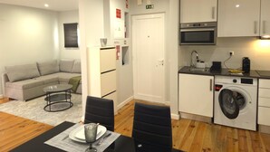Un espace de vie compact comprenant un canapé, une table à manger, des chaises, un lave-linge et une kitchenette.