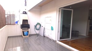 Un balcon carrelé, propre, équipé d’un barbecue, d’un tuyau d’arrosage et d’un chauffe-eau.