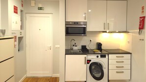 Une cuisine compacte avec des meubles blancs, un four à micro-ondes, un lave-linge et un évier.