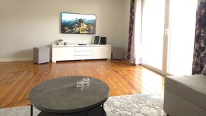 Un salon avec un téléviseur à écran plat fixé au mur, un meuble de rangement blanc, une table basse ronde et un canapé.