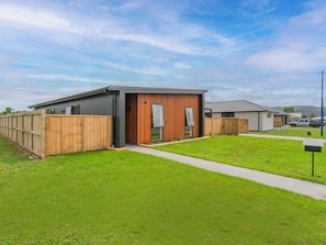 A modern single-story house with a wooden fence, a paved driveway, and a grassy yard.