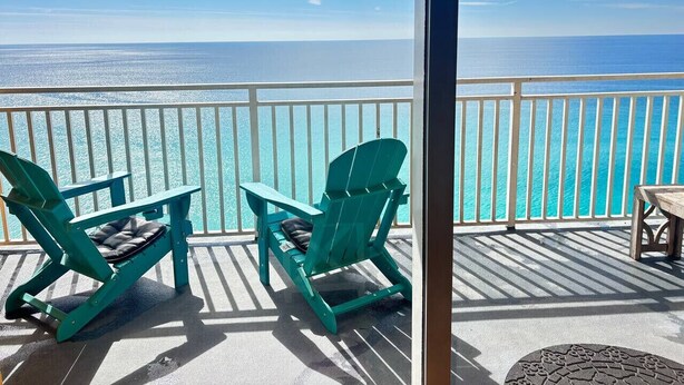 A balcony with two green Adirondack chairs and a small table, overlooking a turquoise ocean. - Splash! Kids Aqua park, Free rental chairs! (Panama City Beach)