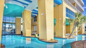 An indoor swimming pool with clear blue water, surrounded by yellow walls and columns, and a palm tree in the corner. - Splash! Kids Aqua park, Free rental chairs! (Panama City Beach)